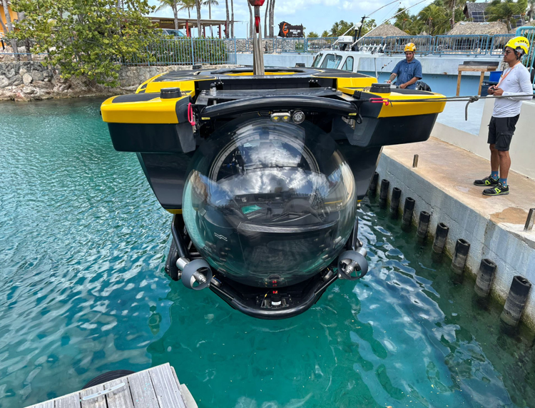 Yellow six-passenger, one-pilot submersible suspended above the water during launch operations